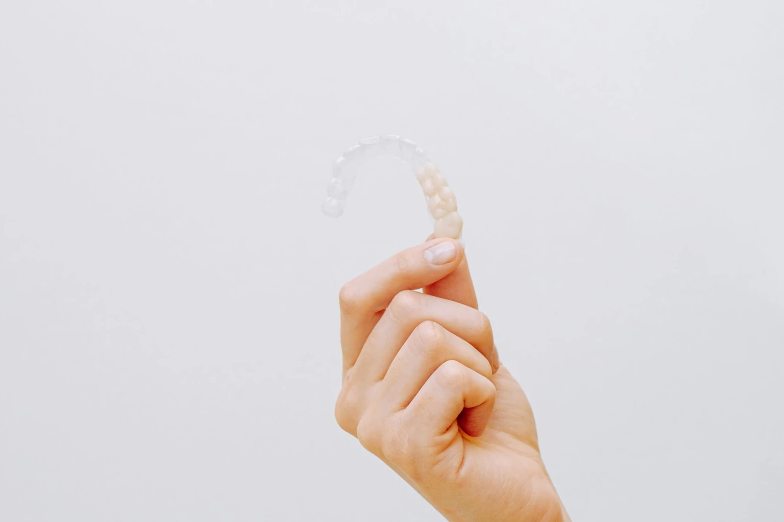 A hand holding a clear dental aligner, prepared for an orthodontic evidence review