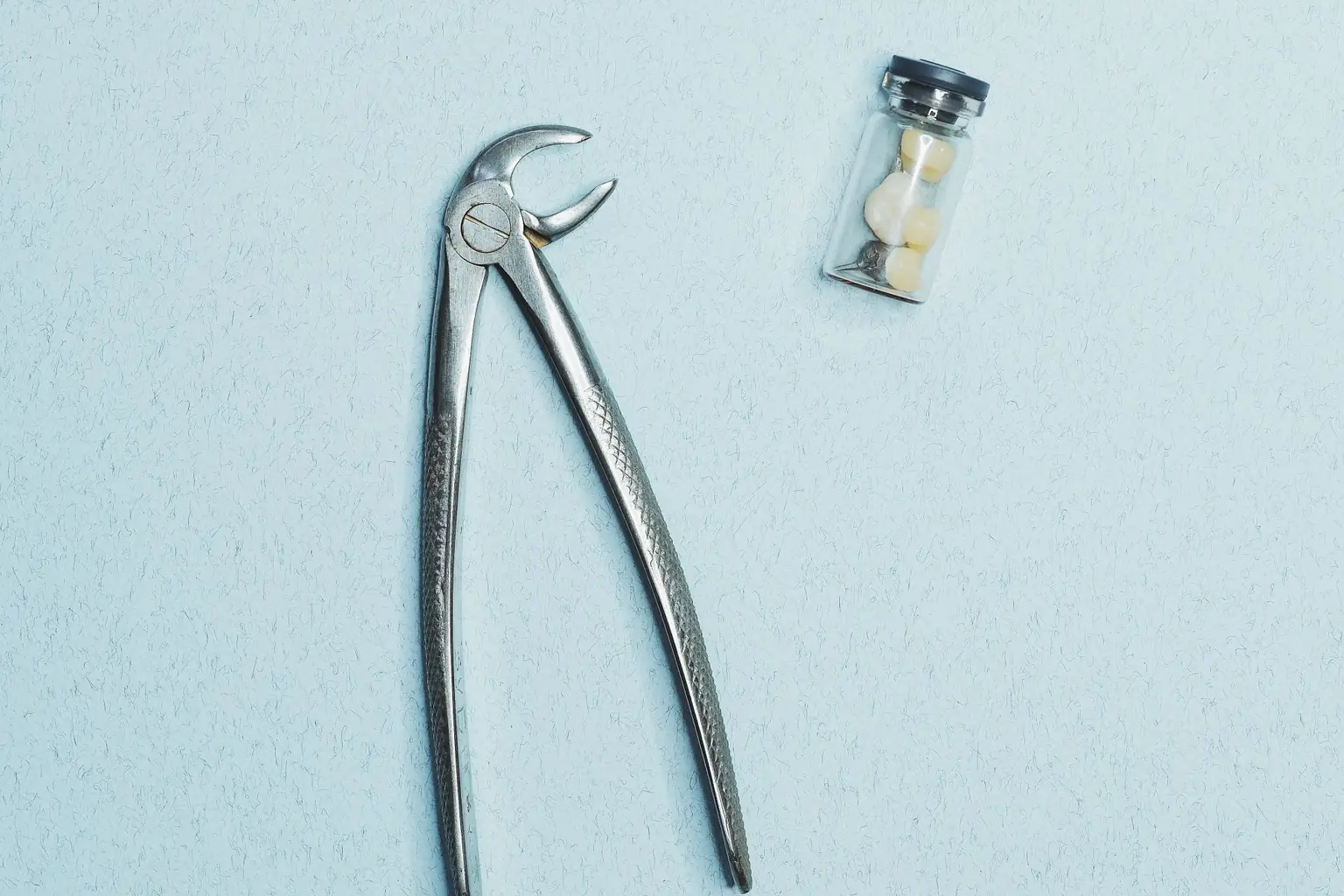 Dental extraction forceps beside a glass vial of extracted teeth, a still-life for a wrong-site extraction review